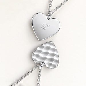 Gros plan de deux pendentifs cœur en argent – face ondulée et dos lisse avec une initiale gravée