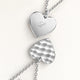 Close-up of two heart-shaped pendants in silver – rippled front and polished back with an engraved initial