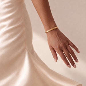 Model in a cream satin dress wearing a personalised gold bangle bracelet with an engraved date