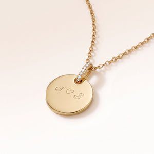 Gros plan d'un pendentif rond en or avec bélière sertie de zircons et gravure personnalisée d'initiales avec un cœur