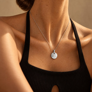 Model in a black ribbed halter top wearing a personalised round silver necklace with white zircons, engraved with initials and a date – room for text, coordinates or handwriting on the back