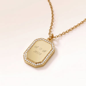 Gros plan d'un pendentif octogonal en or bordé de zircons blancs avec une gravure personnalisée d'initiales, d'un cœur et d'une année