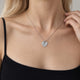 Model in a black top with thin straps touching the chain of her heart-shaped silver necklace with a ridged sunburst pattern and room for personal engraving of text, coordinates or handwriting on the back