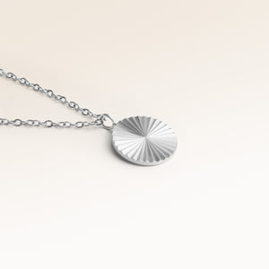Gros plan du pendentif rond minimaliste en argent avec surface rayonnante striée et espace pour gravure au dos