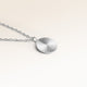 Close-up of minimalist round pendant in silver with ribbed sunburst surface and space for engraving on back