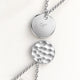 Close-up of two round pendants in silver – rippled front and polished back with an engraved initial